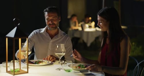Happy elegantly dressed couple is enjoying romantic dinner together and cheering with white wine g