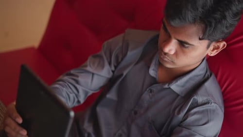Young Adult Using a Tablet on a Red Couch