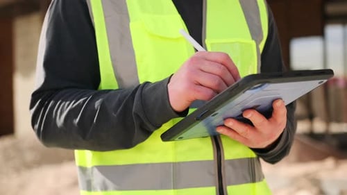 Close up construction worker hands using tablet and stylus, making notes on building blueprints