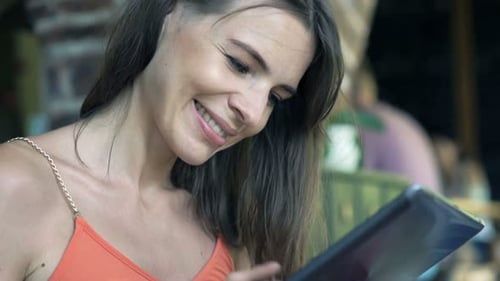 Happy young woman browsing on tablet computer in bright sunny cafe