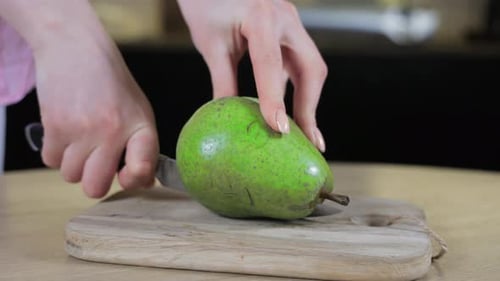 Woman Slicing Ripe Green Pear with Blemishes on Wooden Cutting Board Highlighting Natural Fruit