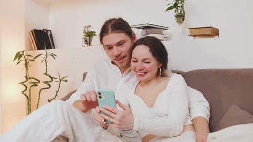 Young Couple Relaxing on Couch Looking at Phone