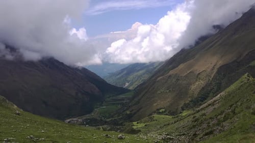 Nach links schwenkendes Panorama auf ein weites grünes Tal, mit Wald bedeckte Hügel mit flauschigen Wolken darüber. Handgerät
