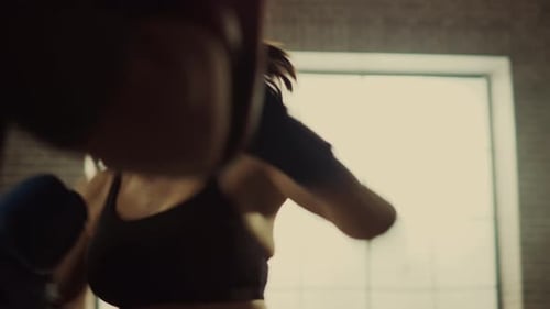 Fit Athletic Woman Kickboxer Punches and Hits the Punching Pads During a Workout in a Loft Gym. She