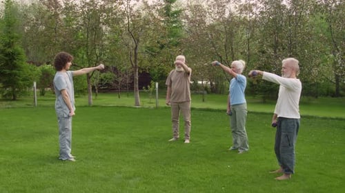 Seniors Exercising with Dumbbells in a Green Field