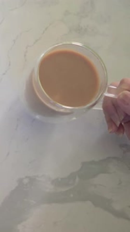 Vertical video: Grasping glass cup, hand with thin bangles shifting it to center on counter to rest