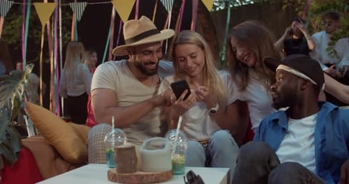 Friends Gather, Look at Phone at Outdoor Party