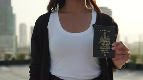 Crop View of Woman Hand Holds Passport of Canada Against Skyscrapers Silhouettes