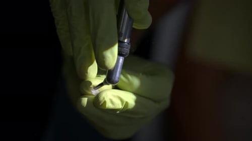 Slow motion close-up of a pair of dentist hands wearing green latex gloves sandblasting a ceramic co