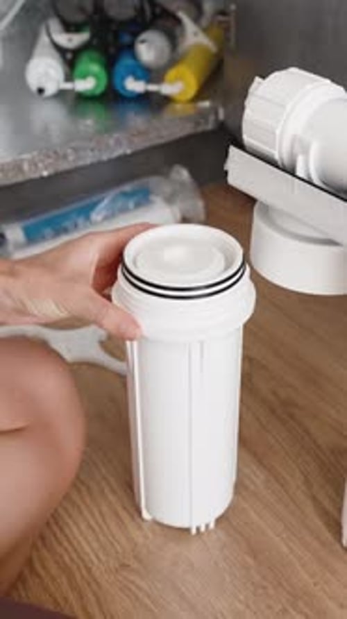 Vertical video. A young woman is sitting on the kitchen floor and replacing water filters.