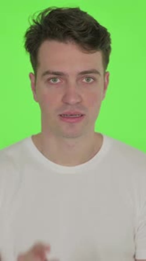 Glücklicher junger Mann, der auf grünem Hintergrund in die Kamera zeigt, vertikales Video