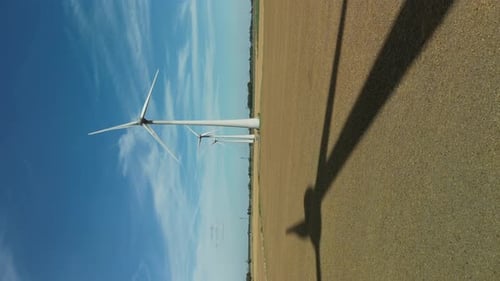 Vertical video drop shadow of a rotating wind turbine in a field on a sunny day