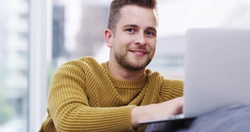 Young Man Smiling While Using Laptop at Home