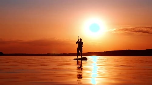 Man Paddle Boarding on Water at Sunset