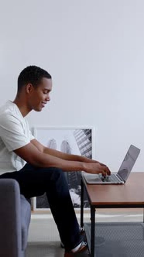 Side View of Young Millennial Student Working on Laptop Sitting on Sofa at Home