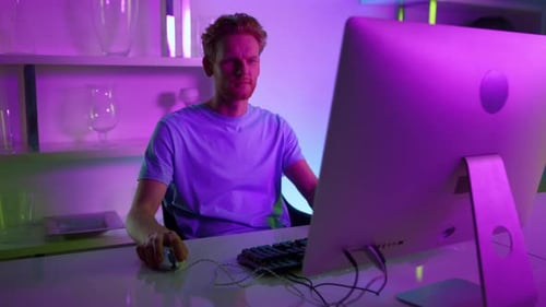 Neonmann schaut auf Computerbildschirm und arbeitet zu Hause. Konzentrierte Spieler genießen den Abend