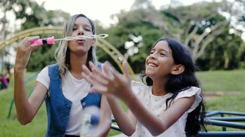Family, Happy hispanic mother and daughter play blowing soap bubbles at park city