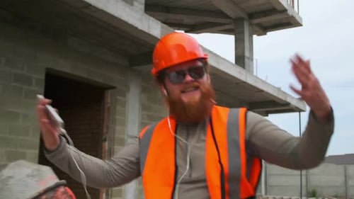 Close-up do carismático engenheiro construtor, trabalhador barbudo, curtindo música em fones de ouvido, dançando