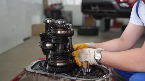 Mecânico de automóveis: a transmissão manual conserta o garfo da caixa de câmbio na estação de serviço usando luvas