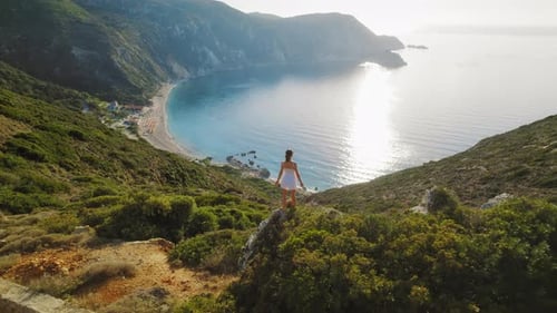 Woman standing on a hilltop overlooking Petani Beach in sunny summer Kefalonia