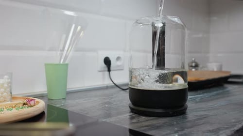 Water Pouring Into Glass Jar on Kitchen Counter with Blurred Background