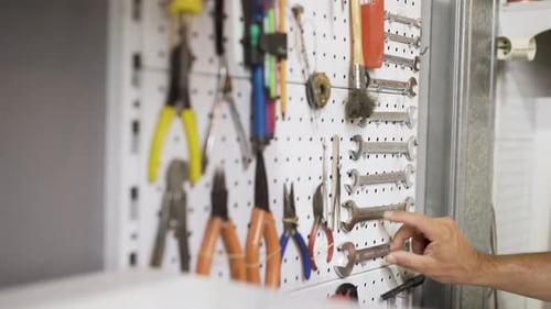 Close up of caucasian mechanic worker male choosing the right wrench tool from a tools board in gara