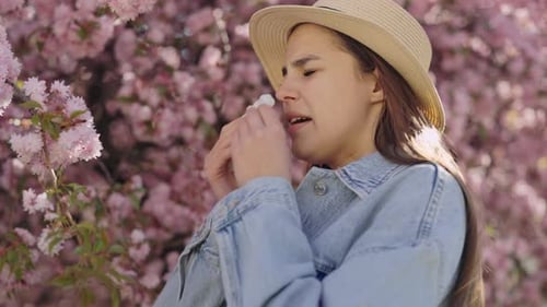 Side View of Young Woman with Runny Nose From Pollen Sneezing in Napkin Outdoors