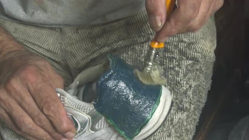 Der Schuhmechaniker repariert die zerrissene Rückseite von Sneakers, indem er sie festklebt