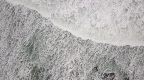 Stormy sea with waves breaking, white foam and beach sand dragged into the sea