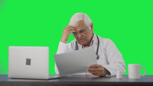 Confused Indian senior doctor reading health reports Green screen
