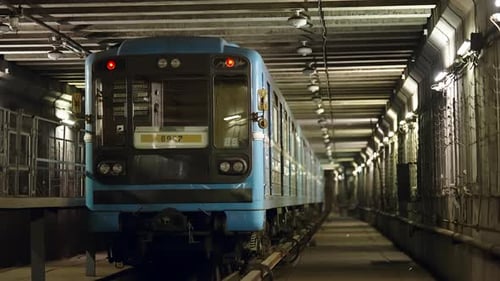Blaue U-Bahn nähert sich in einem beleuchteten unterirdischen Tunnel, frontal zwischen Betonbalken betrachtet
