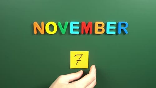 Hand sticking a sticker 7 November calendar day on school board. 7 date of November. Seventh day