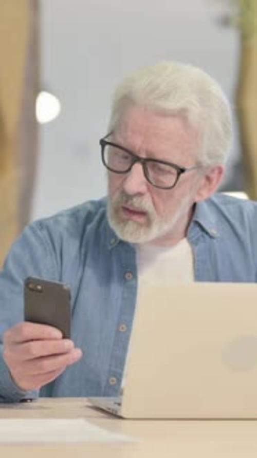 Senior Man Using Smartphone and Laptop Indoors
