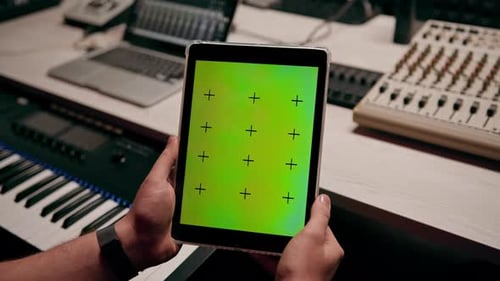 professional recording studio sound engineer holding tablet with green screen near equalizer mixer