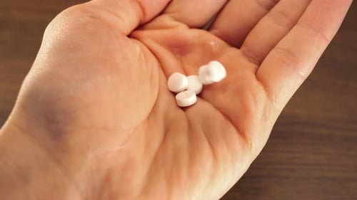 Weiße Pillen (Medikamente), die aus einem weißen Behälter in die Handfläche fallen