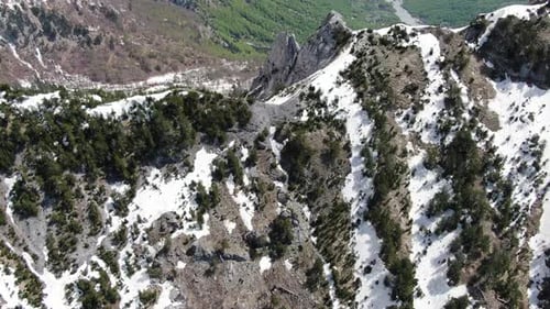 Vista de un Zumbido en Albania volando en los Alpes que muestra un pico montañoso nevado y rocoso entre dos f verdes