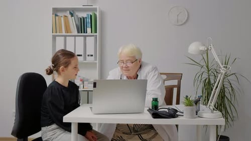 Ein Arzt in weißer Uniform mit einer Patientin zeigt beim Termin ein Röntgenbild auf einem Laptop.