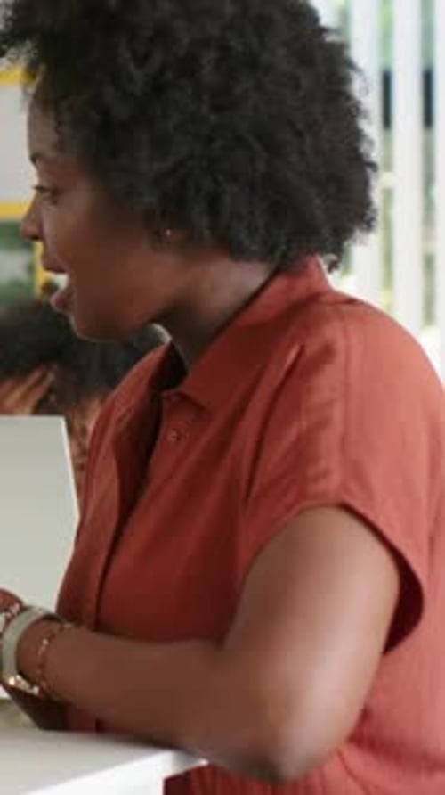 Vertical video: Showing teacher in rust shirt holding paper, finger counting at desk with laptop