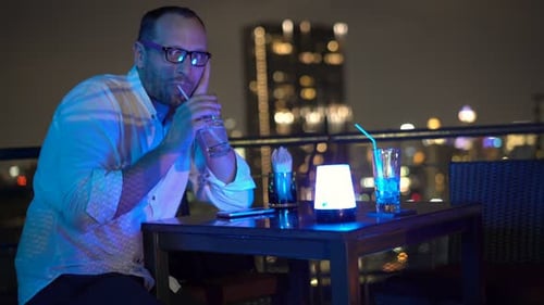 Portrait Of Happy Man Drinking And Raising Toast On Terrace In Bar At Night