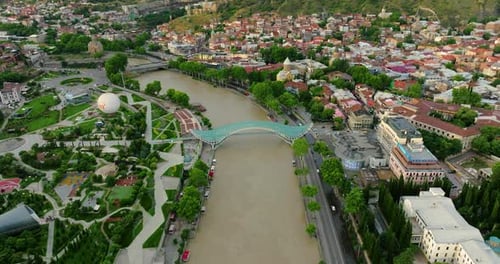 Bow-shaped Pedestrian Bridge Of Peace Over The Kura River In Tbilisi, Georgia. Aerial Shot