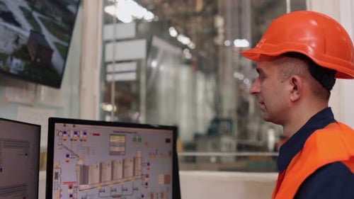 Factory Worker Examining Computer Monitors in a Workplace