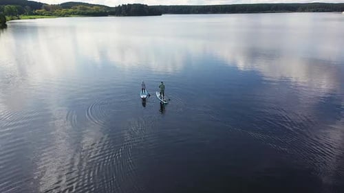 Tourists Stand Up Paddling on Calm Lake with Cloudy Sky Reflection