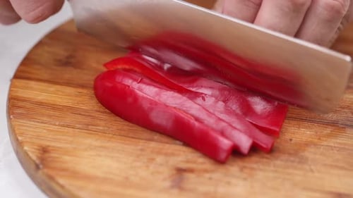 Close up of hands using knife slicing red bell pepper on wooden cutting board