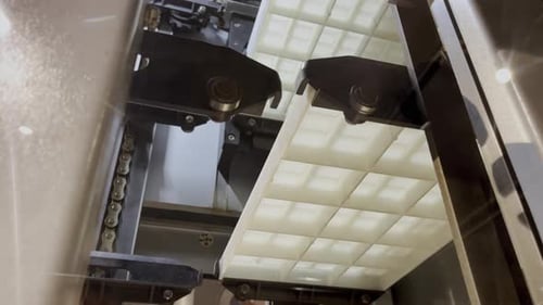 Des moules en plastique blanc circulent sur une chaîne de montage dans une usine