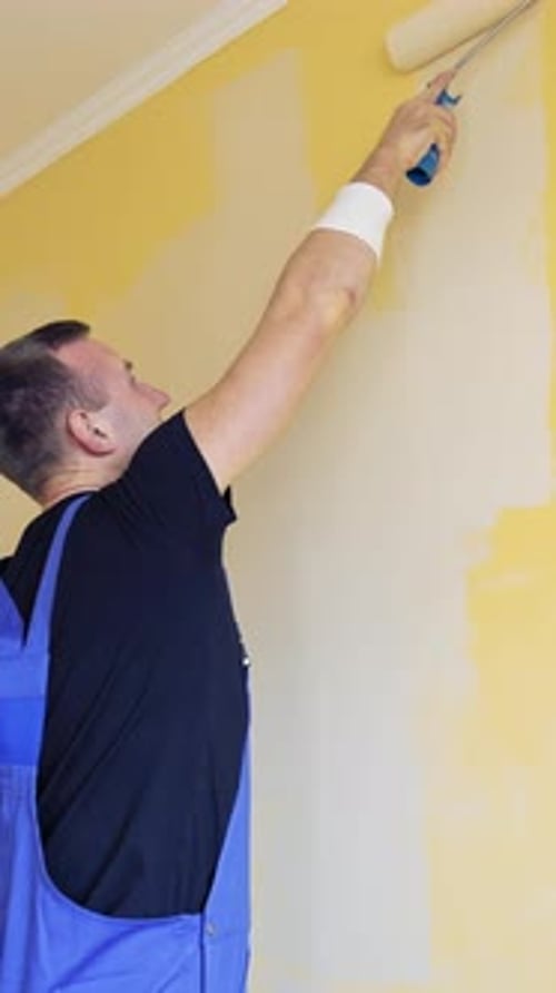 Room renovations at house. Paint being applied on a wall by a professional worker.