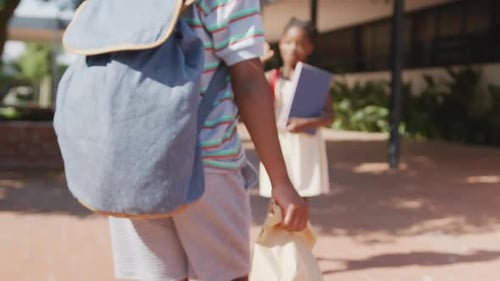 Video of happy african american boy and girl with schoolbags high fiving outside school