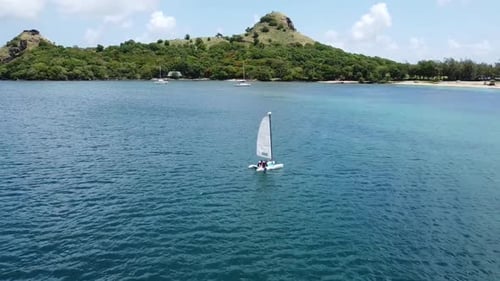 A aerial view of a small sailboat in the blue of the Caribbean waters on a sunny day.