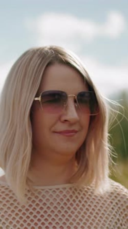 Femme d'affaires souriante aux lunettes de soleil marchant à l'extérieur sous un ciel ensoleillé