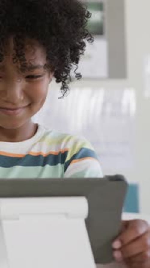 Vertical video: Reading child in striped tee studying tablet in case in class as screen showing app