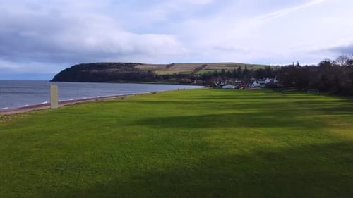 A serene coastal scene with a large stone monument standing tall on a grassy field. In the distance,